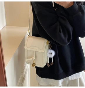 Detail der cremefarbenen Handytasche mit Plüsch-Anhänger und goldenem Logo am Modell