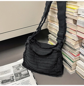 Detail of black canvas crossbody bag with unique frayed edges and pleated texture