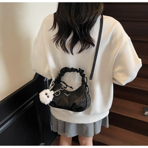 Détail du sac à bandoulière plissé noir avec anse à volants et breloque en peluche blanche
