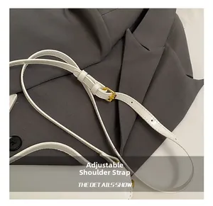 Close-up of adjustable white leather shoulder strap with gold buckle on a suit jacket