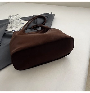 Close-up of vintage dark brown faux suede tote bag on white bedding in minimalist setting