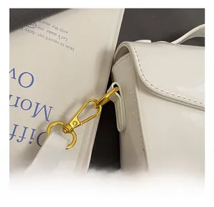 Close-up of golden metal clasp on white patent leather handbag with luxury chain strap