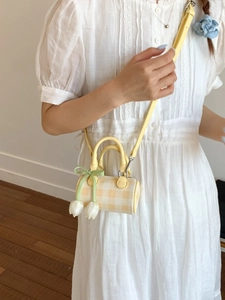 Mini yellow checkered cylinder crossbody bag with tulip charms on white lace dress
