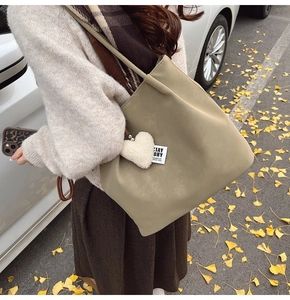 Detail of khaki green faux leather tote bag with heart plush charm in autumn street setting