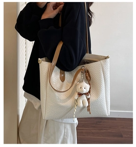 Detail view of white tote bag featuring woven texture and a cute bear bag charm