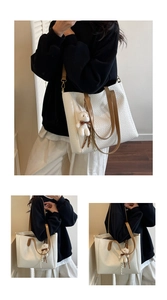 Detail view of white woven tote bag with brown leather handles and bear charm accessory