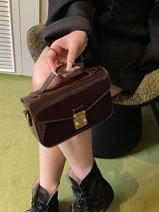 Retro dark brown patent leather crossbody bag with gold buckle shown on a green rug