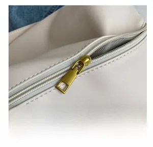 Macro shot of smooth bronze zipper and fine stitching on cream leather shoulder bag
