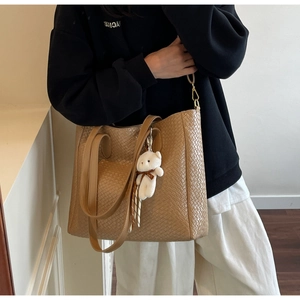 Brown woven texture tote bag shown on shoulder with cute bear pendant detail