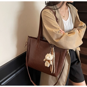 Detail of dark brown woven tote bag with adjustable shoulder strap and cute plush charm