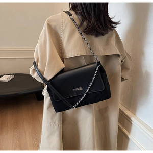 Dettaglio di una borsa tote nera in pelle con catena e logo indossata da una modella