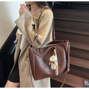Detail of dark brown woven tote bag with adjustable strap and cute bear charm accessory