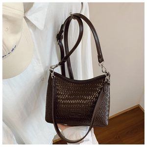Detail of dark brown woven bucket bag with metal hardware and thin leather strap