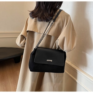 Dettaglio della borsa nera in pelle scamosciata con catena e targhetta logo in metallo