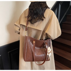 Detail of dark brown woven leather tote bag with a white bear plush charm on a shoulder strap