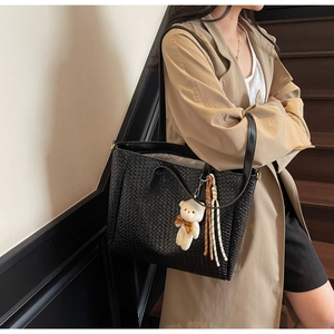 Detail of black woven tote bag featuring a cute white bear charm and sturdy shoulder straps
