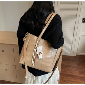 Detail of khaki woven tote bag with texture, plush bear charm and adjustable strap