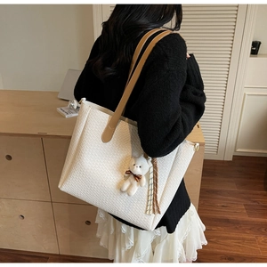 White woven tote bag detail showing large capacity, plush bear charm, and brown straps