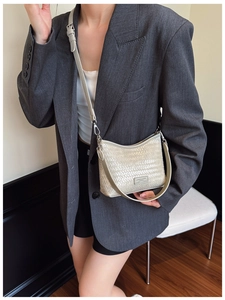Detail view of beige woven bucket bag with metallic logo plate and adjustable shoulder strap