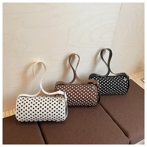 Three minimalist polka dot barrel bags in black, white, and brown on a soft bench