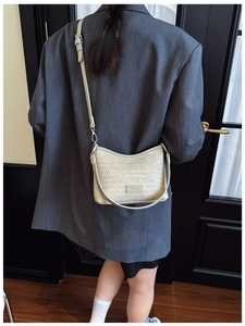 Detail of beige woven leather bucket bag worn with a grey suit for a classic look