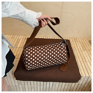 Detail of brown cylinder bag with white polka dots featuring an adjustable shoulder strap