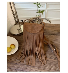 Gros plan du sac bandoulière en daim marron avec de longues franges sur bois vintage