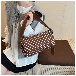 Close-up of brown polka dot bolster bag with wide leather strap and silver rivet details
