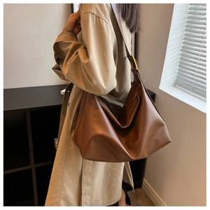 Detail of a pleated brown leather tote bag with a golden adjustable buckle strap