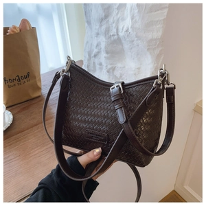 Detail of a dark brown woven leather bucket bag with silver buckles and a fashion label