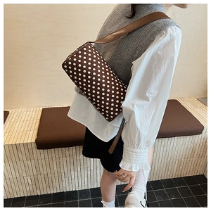 Side view of a brown polka dot cylinder shoulder bag worn by a model in a minimalist room
