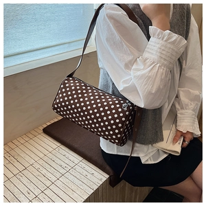 Detailed view of dark brown polka dot cylinder bag with top zipper and slim shoulder strap