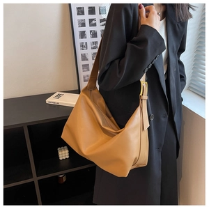 Close-up of a brown leather tote bag with wide shoulder strap and gold buckle detail
