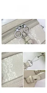 Detail of lace embroidery, metal zipper pull and silver strap buckle on beige box bag