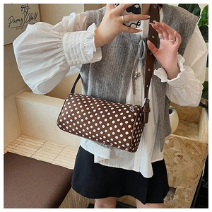 Detailed view of the brown polka dot cylinder bag with leather strap worn by a model