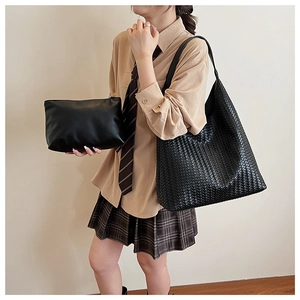 Close-up of black woven tote bag and smooth leather clutch set shown on a model