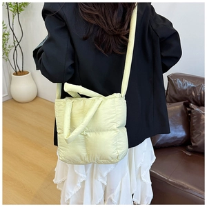 Detail of light yellow quilted down handbag with square padded texture and wide shoulder strap