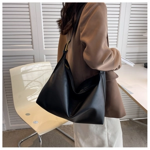 Side view of a large black hobo shoulder bag with a gold metal buckle on brown blazer
