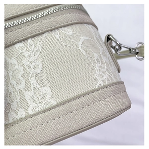 Detail shot of the beige crossbody bag featuring white lace floral texture and silver zipper