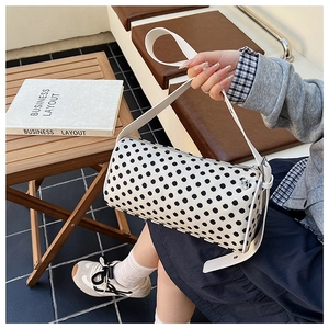 Close-up of white polka dot cylinder shoulder bag with adjustable leather strap