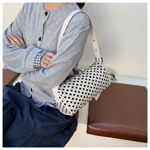 Close-up of a white polka dot cylinder shoulder bag with silver buckles and leather strap