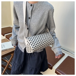 Detailed view of polka dot cylindrical crossbody bag worn over a gray cardigan