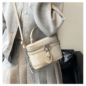 Detail of cream barrel bag featuring white lace embroidery and double ring zippers