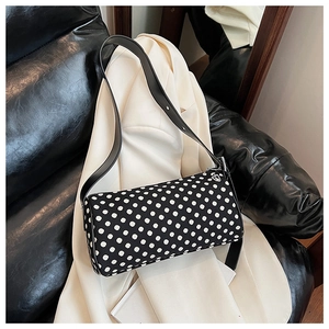 Close-up of a stylish polka dot pillow bag on a leather sofa with a white blazer