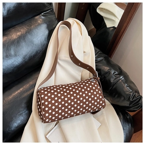 Detail of brown polka dot barrel bag with silver studded leather strap on white fabric