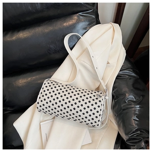 Detailed view of the black and white polka dot cylindrical pillow bag on a beige blazer