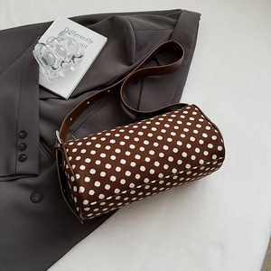 Chic brown polka dot cylinder pillow bag with adjustable leather strap on a grey suit jacket