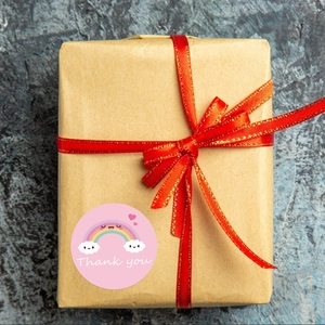 Detail of rainbow thank you sticker on brown paper gift box with red ribbon decoration