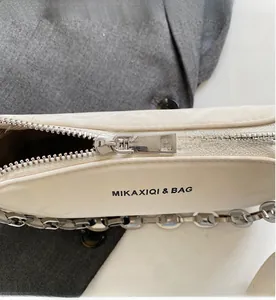 Close-up of silver metal zipper and chunky chain on creamy white leather shoulder bag
