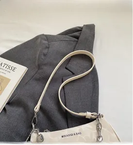 Detail of cream shoulder bag with stone texture and silver chain on a grey blazer